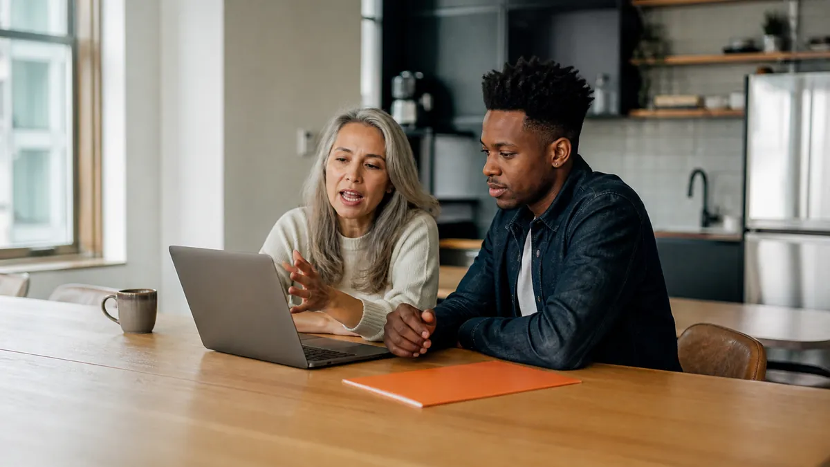 Two colleagues comparing voice dictation app plans at a laptop in a bright shared kitchen workspace